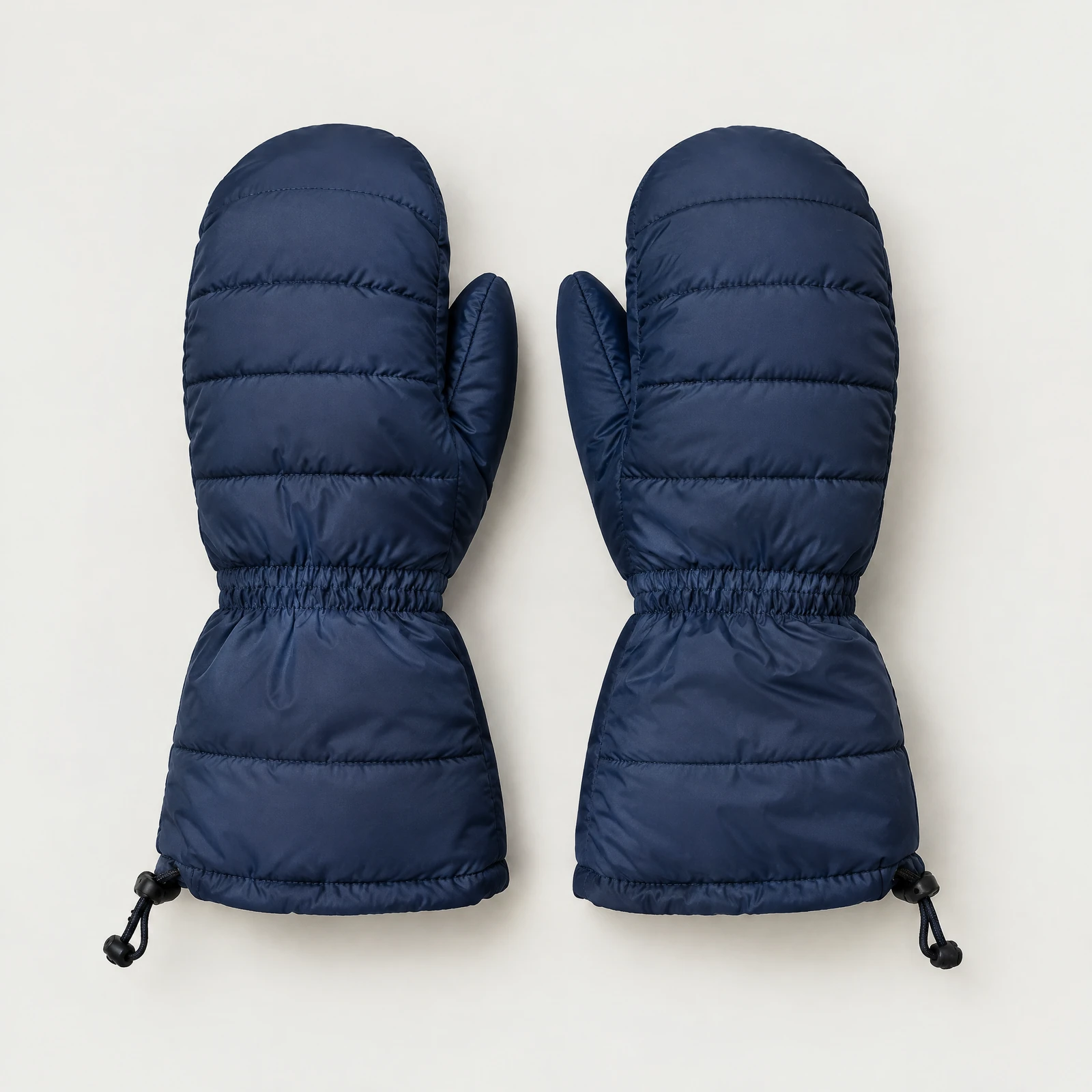 One pair of navy quilted mittens with long cuffs and cord pulls laid flat on a light gray background